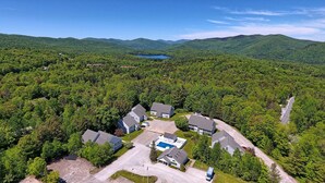 An aerial view of a residential area with houses, a swimming pool, and a lake in the background.