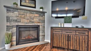 A modern living room with a stone fireplace, a flat-screen TV mounted above it, and a wooden cabinet.