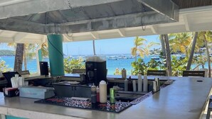 An outdoor bar area with a view of the ocean, equipped with bar stools and a coffee machine. - Cowpet Bay Beach Front Villa with Amazing Views (Elysian Beach Resort)