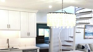 A modern kitchen with white cabinetry, a marble island with bar stools, and a unique chandelier. - Cowpet Bay Beach Front Villa with Amazing Views (Elysian Beach Resort)