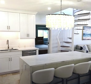 A modern kitchen with white cabinetry, a marble island with bar stools, and a unique chandelier. - Cowpet Bay Beach Front Villa with Amazing Views (Elysian Beach Resort)