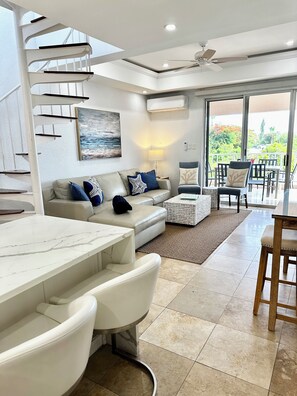 A modern living area with a white sofa, a marble coffee table, and a dining area with a wooden table and chairs.