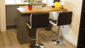 A compact kitchen with modern appliances, two bar stools, and a small potted orchid on the counter. - Studio l'Orchidée Mobility lease (1 to 10 months) (Rueil-Malmaison)