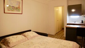 A bedroom with a bed, a small kitchenette, and a door leading to another room. - Studio l'Orchidée Mobility lease (1 to 10 months) (Rueil-Malmaison)