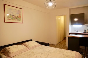 Une chambre avec un lit, une petite kitchenette et une porte donnant sur une autre pièce.