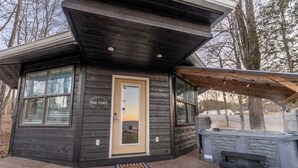 A small cabin with a wooden exterior, a door with a window, and a bench outside.