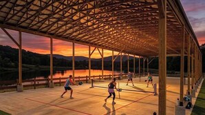An outdoor tennis court with a wooden pavilion structure, surrounded by a natural landscape.
