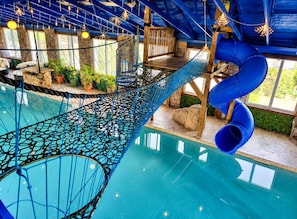 A pool area with a rope bridge, slides, and wooden structures.