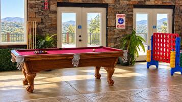 Une table de billard dans une pièce aux murs en pierre, avec vue sur un paysage montagneux.