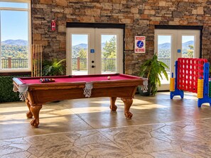 Une table de billard dans une pièce aux murs en pierre, avec vue sur un paysage montagneux.