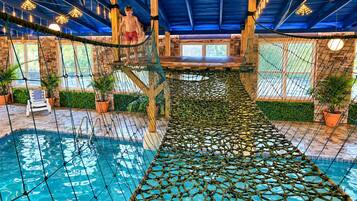 Un espace piscine intérieure doté d’un pont suspendu au-dessus de l’eau, de poutres en bois et de plantes en pot.
