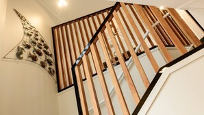 En trappe i træ med et moderne design, en spiraltrappe i baggrunden og en dekorativ vægdekoration.
