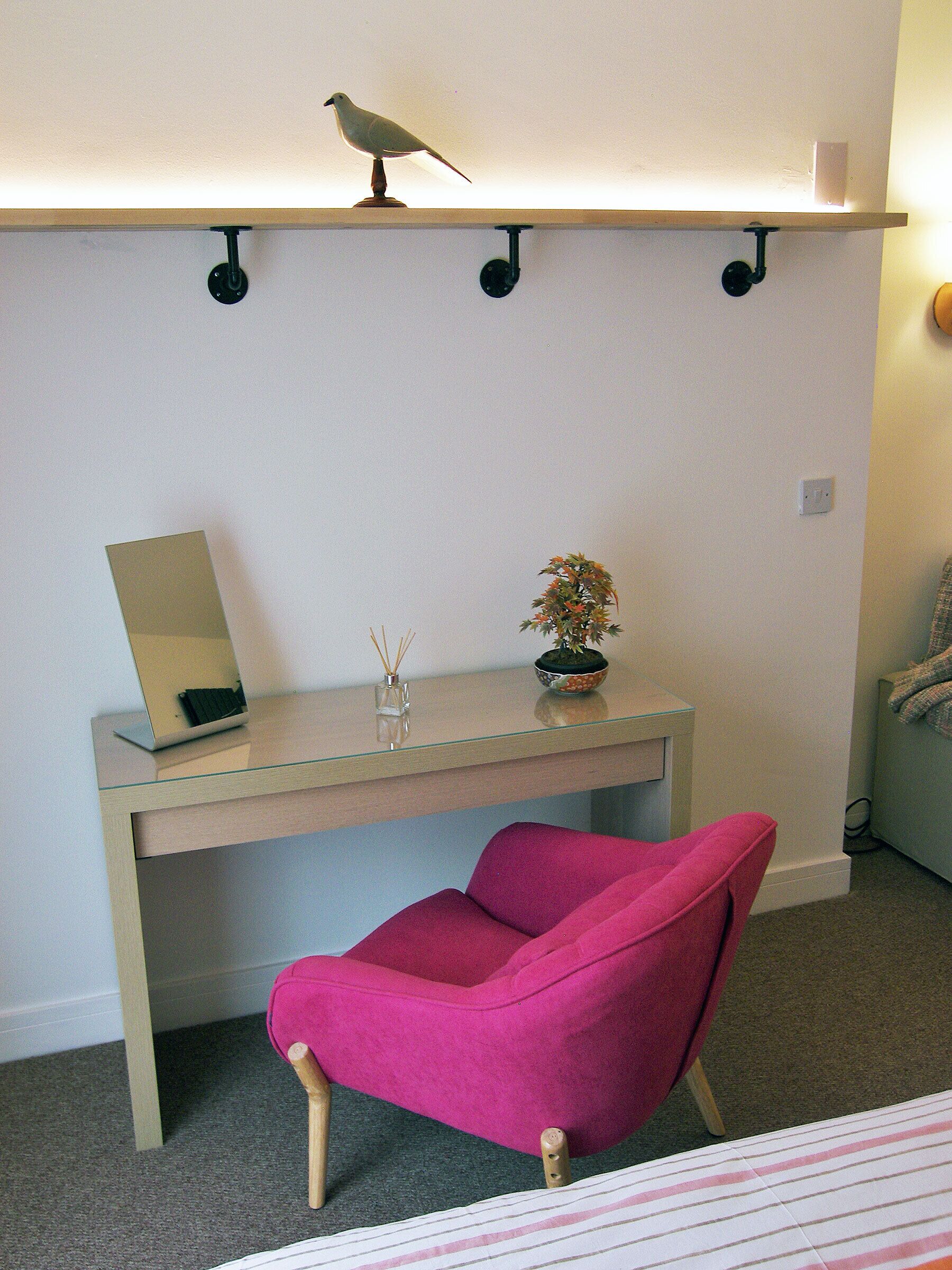 A room with a desk, a chair, a shelf with a bird, and a small plant.