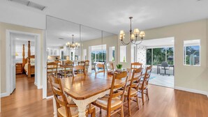 A spacious dining area with a large wooden table and chairs, a chandelier, and a view of the kitchen and living area through large windows. - Sarasota Waterfront Paradise- Location, Location...!!
 (Sarasota)