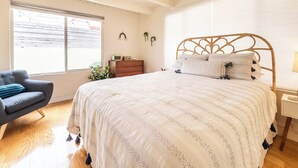 A bedroom with a large bed, a chair, a dresser, and a window.