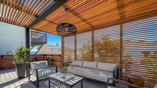 An outdoor patio with a wooden pergola, a sofa, a table, and chairs.