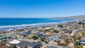 A coastal residential area with houses, a clear blue sky, and the ocean in the background.