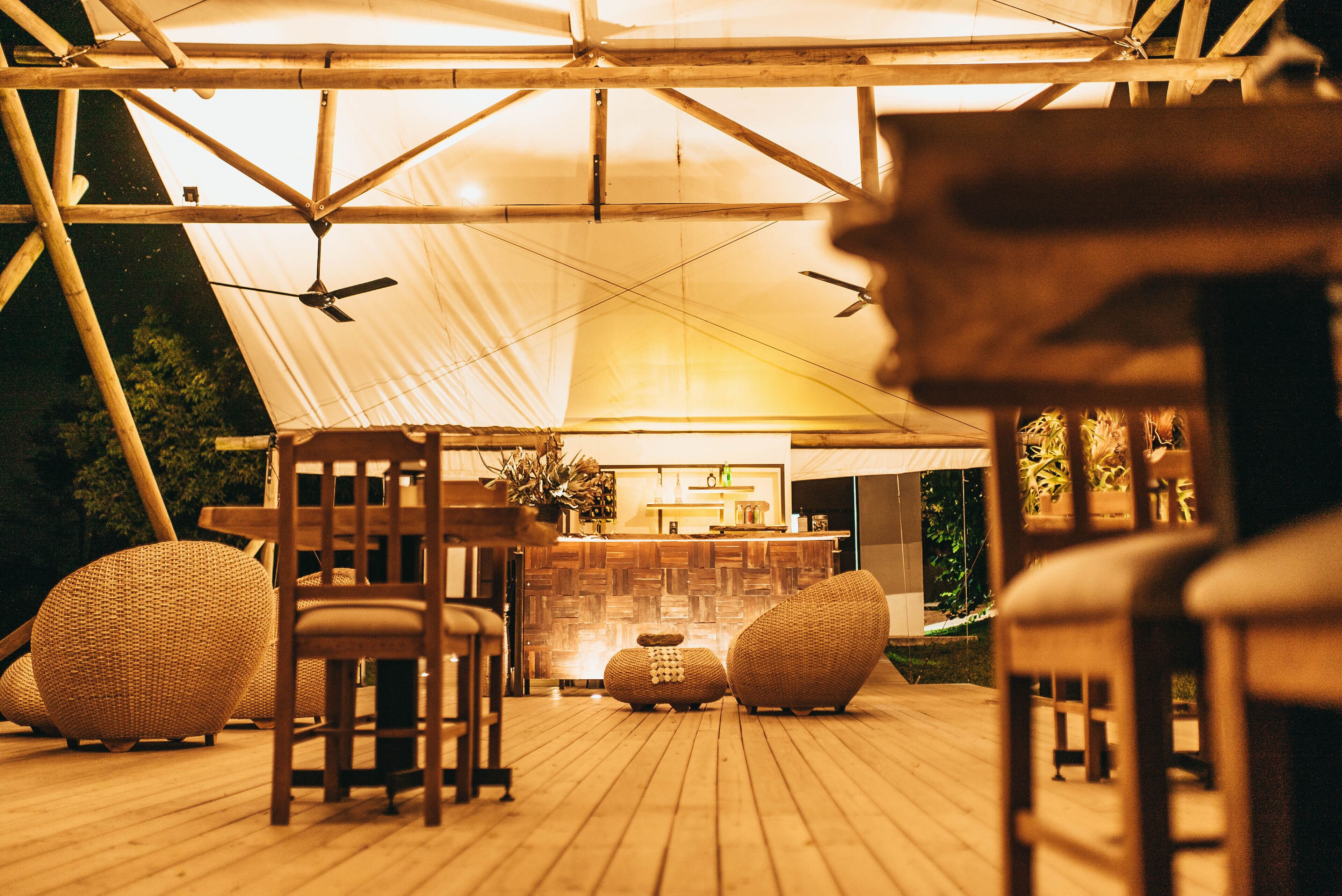 Un área de comedor al aire libre con mobiliario de madera y una barra bajo una gran carpa.