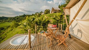 Una terraza de madera con un jacuzzi, una mesa con platos y una tienda de campaña.