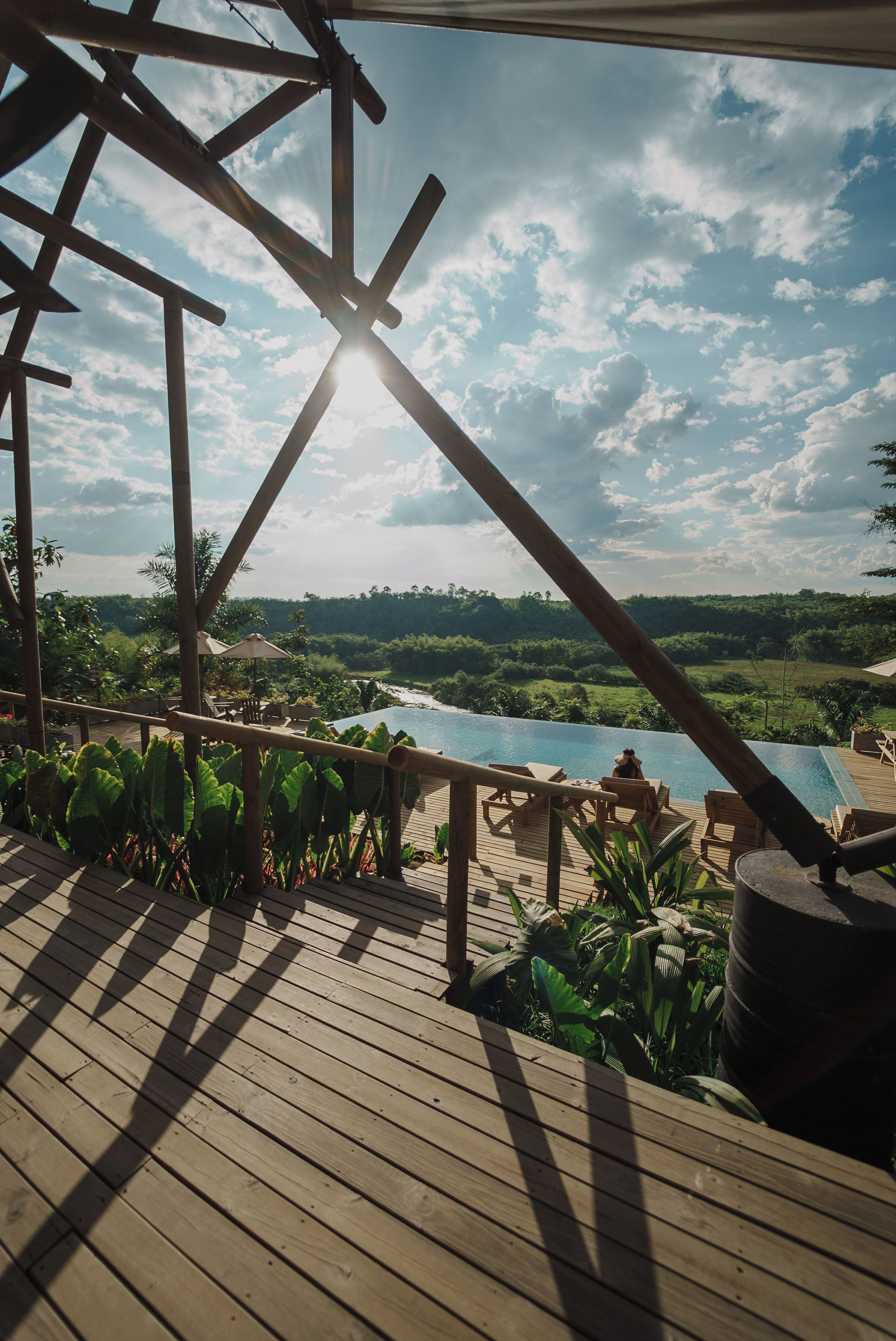 A wooden deck with a pool and lounge chairs, overlooking a lush landscape.