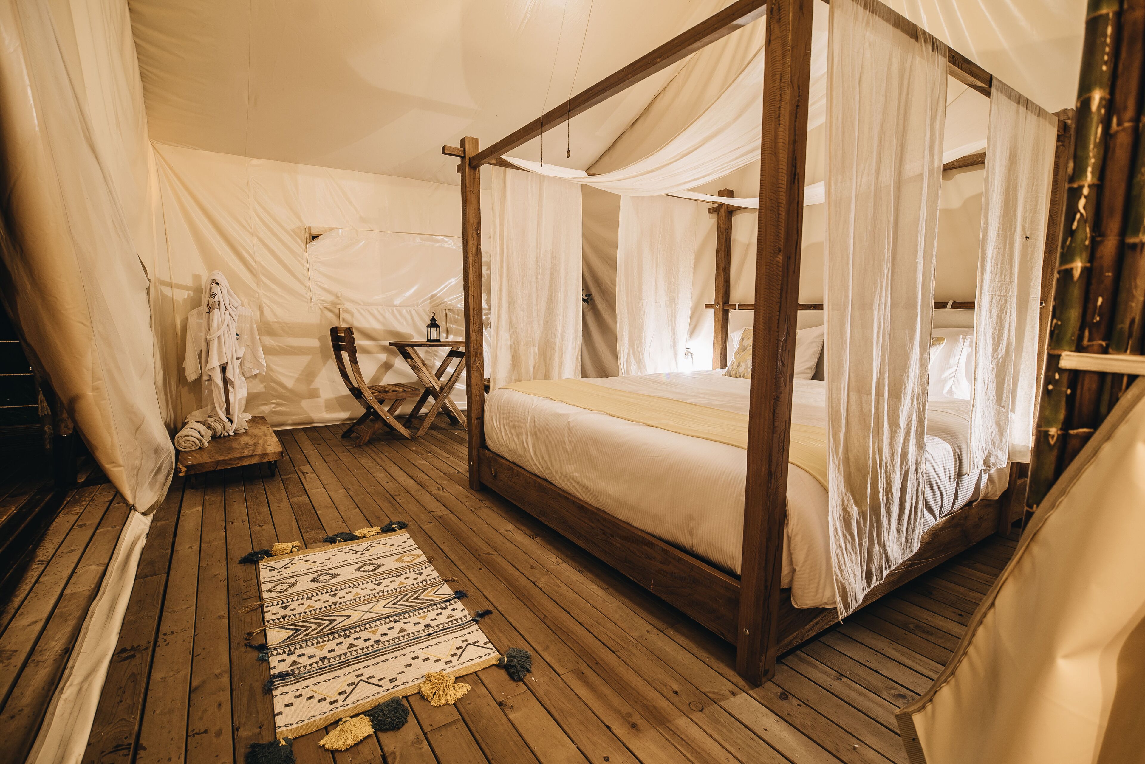 A four-poster bed with a canopy, wooden flooring, and a patterned rug.
