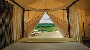 Tienda de campaña con cama y vista a un río y bosque.