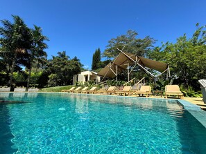Una piscina azul cristalina con sillones de descanso y una zona sombreada.