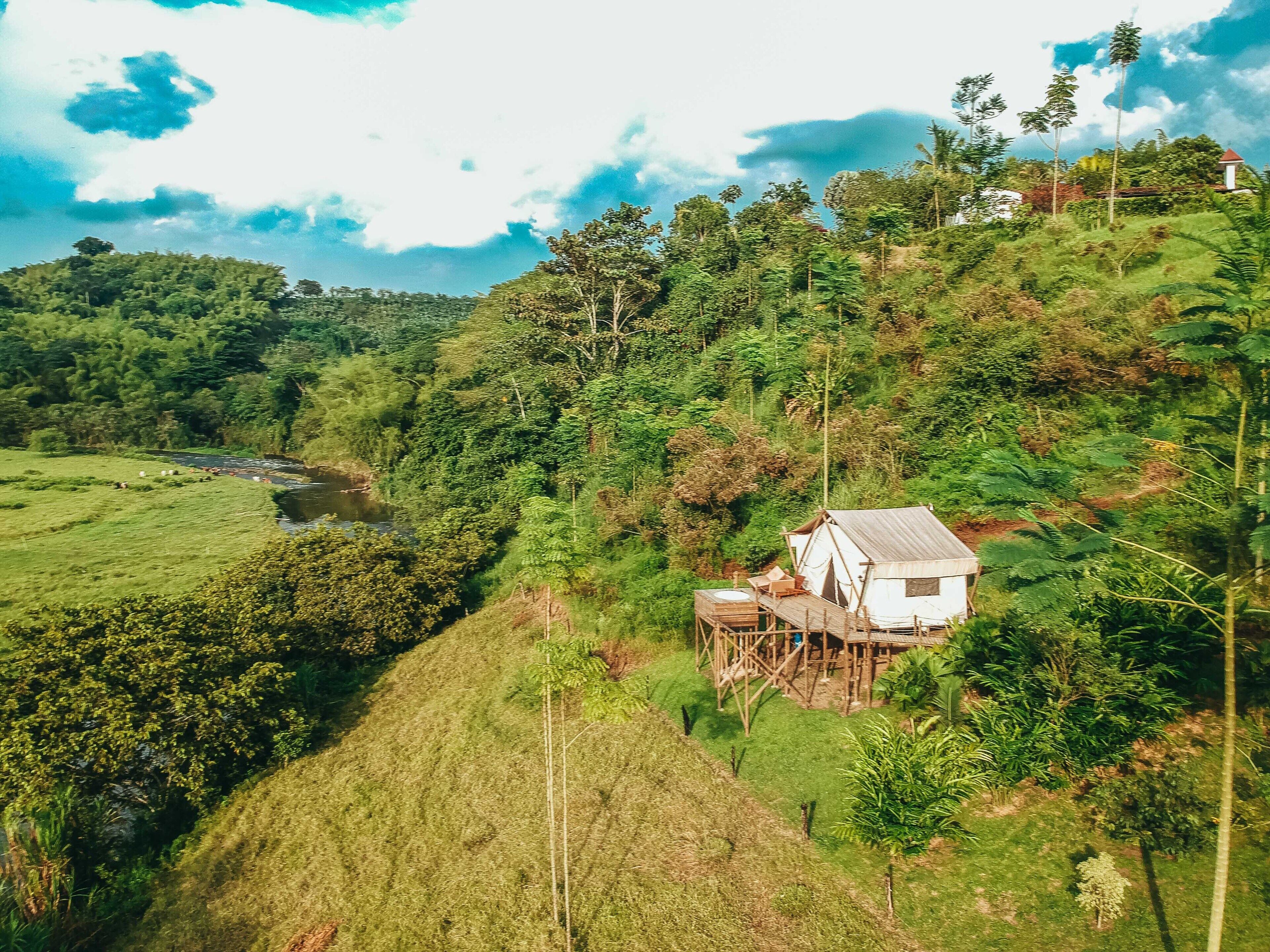 A white house with a wooden deck, surrounded by lush greenery and a river in the background.
