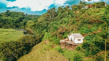 A white house with a wooden deck, surrounded by lush greenery and a river in the background.