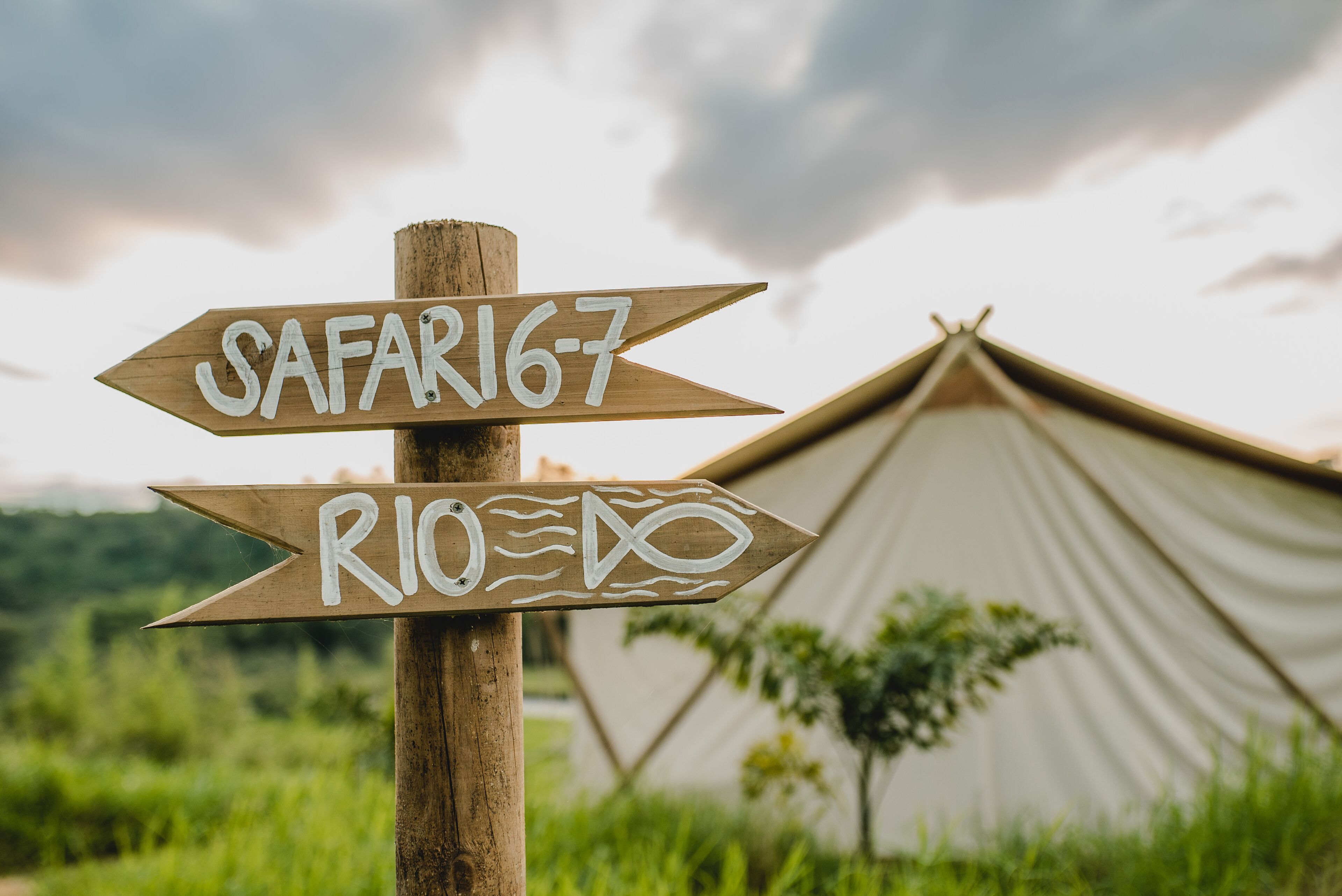 A wooden signpost with directions to 'SAFARI 6-7' and 'RIO DO' with a tent in the background.