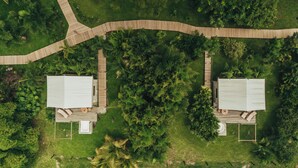 Vista aérea de una propiedad con dos cabañas, cada una con un balcón y un pequeño porche, rodeadas de abundante vegetación y un sendero de madera.