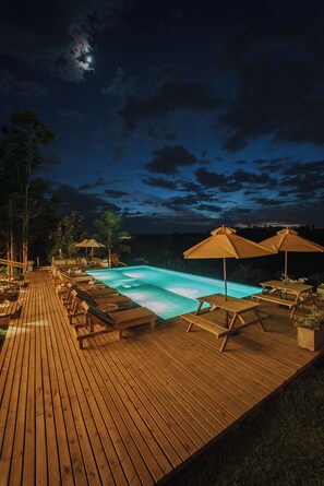 Terraza de madera con sillones de descanso y sombrillas que da a una piscina.