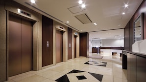 A hotel lobby with a modern design, featuring a central elevator, a reception desk, and a patterned floor. - Keio Presso Inn Shinjuku (Tokyo)