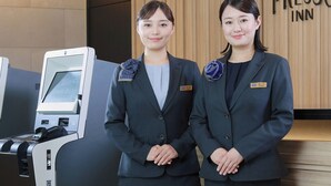 Two individuals in business attire standing in front of a reception desk with a nameplate and a digital kiosk. - Keio Presso Inn Shinjuku (Tokyo)