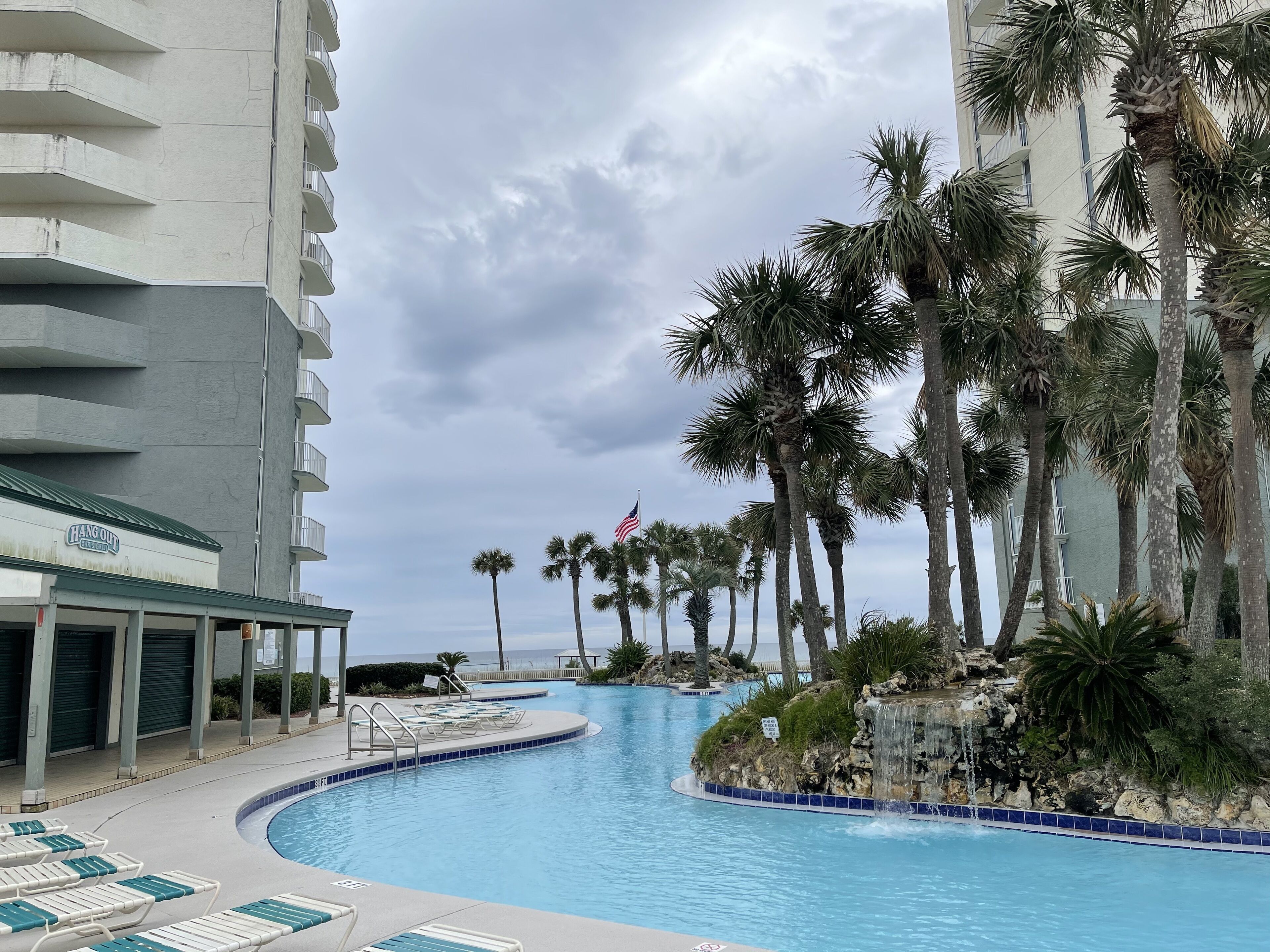 A swimming pool with lounge chairs, palm trees, and a building with balconies.