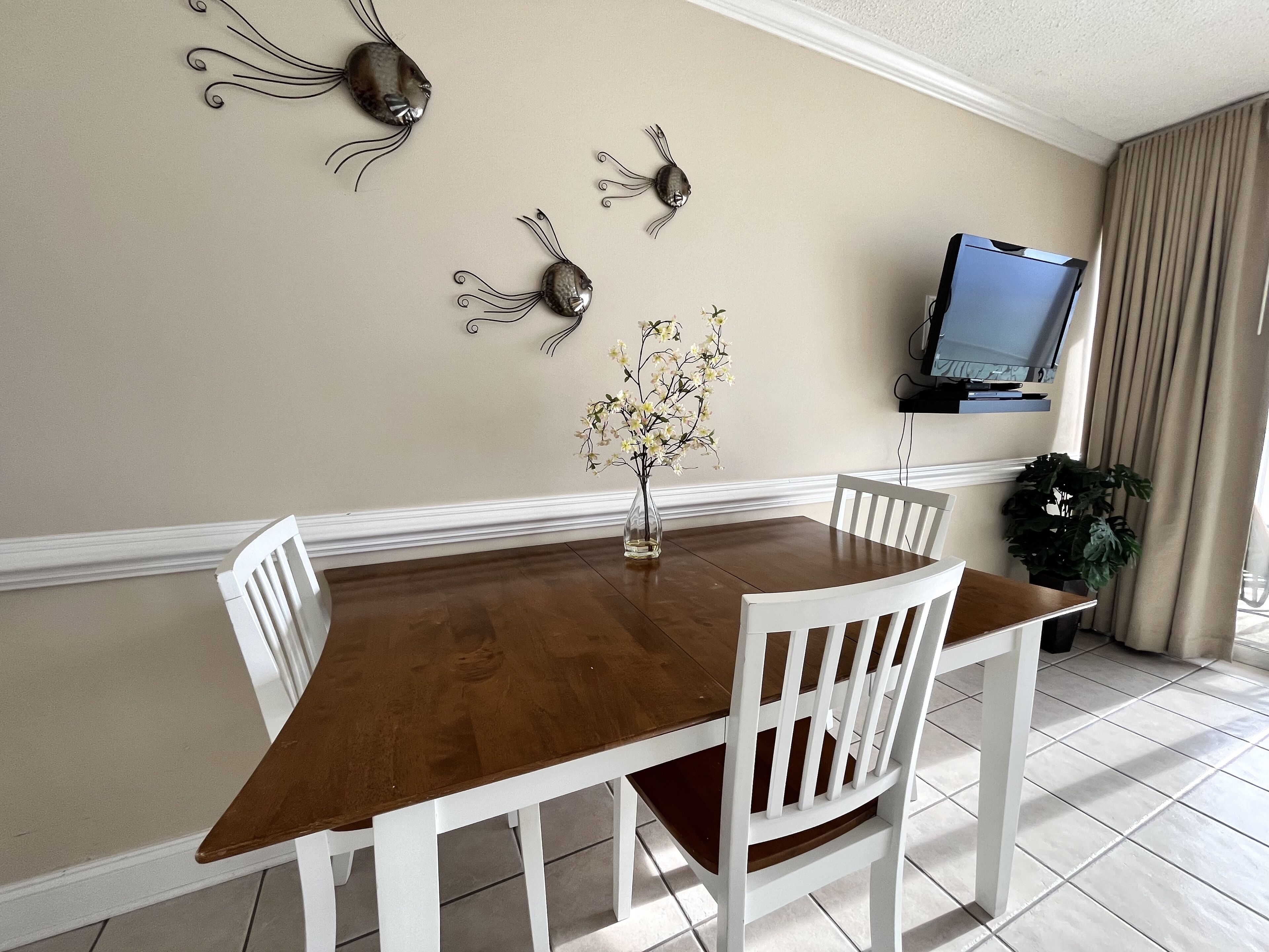 Un coin repas avec une table en bois et des chaises blanches, un vase rempli de fleurs et des éléments décoratifs en métal fixés au mur.