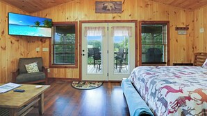 Een houten kamer met een bed, een sofa, een televisie en een eethoek met stoelen.