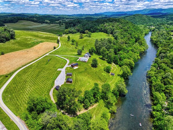 Vista aérea de una zona rural con un río, campos verdes y varias casas.