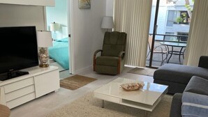 Een moderne woonkamer met een flatscreen televisie, een grijze bank, een salontafel en een groene fauteuil.