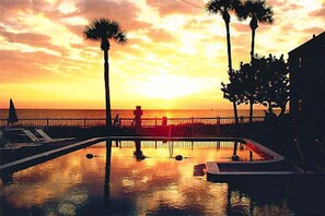 Vista al atardecer sobre una piscina, con palmeras y una valla.