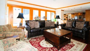 A living room with a leather sofa, patterned armchairs, a wooden coffee table, and a red and white patterned rug.