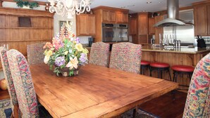 A wooden dining table with floral centerpiece, patterned chairs, and a chandelier.