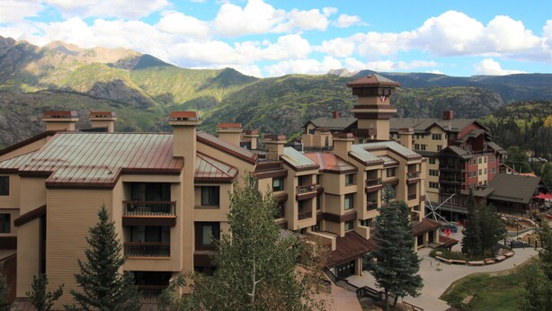 A multi-story hotel with a central tower, surrounded by mountains and trees.