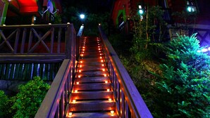 Un escalier en bois, illuminé, mène à un bâtiment dont le toit est rouge.