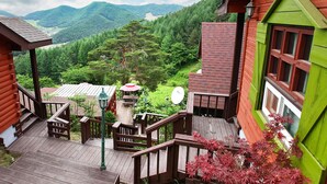 Une cabane en bois dotée d’une terrasse en bois et d’un escalier menant à un espace abrité sous un parasol rouge.