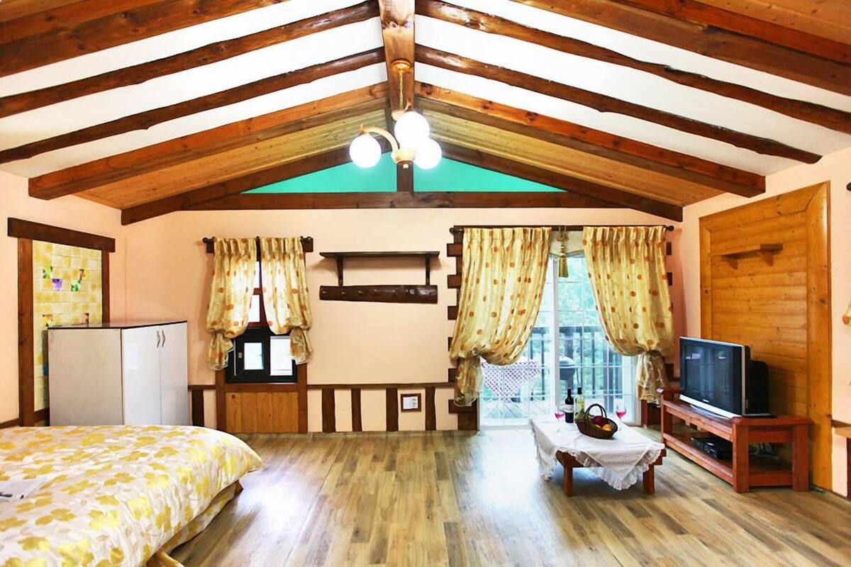 A cozy room with wooden beams, a bed, a table with a vase, and a television.