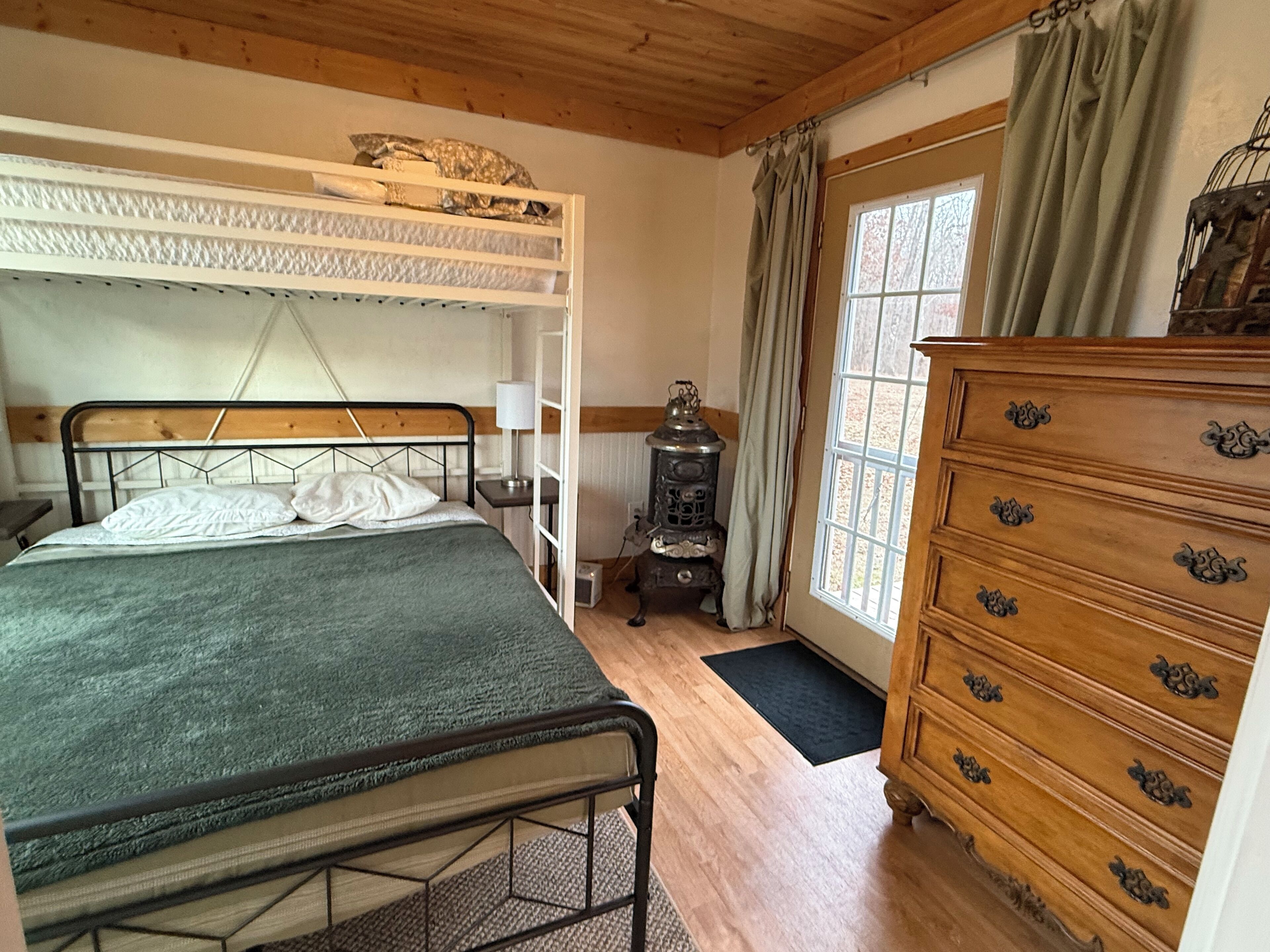 A bedroom with a bunk bed, wooden dresser, and a window with curtains.