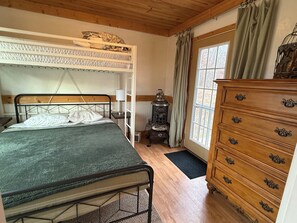 A bedroom with a bunk bed, wooden dresser, and a window with curtains.