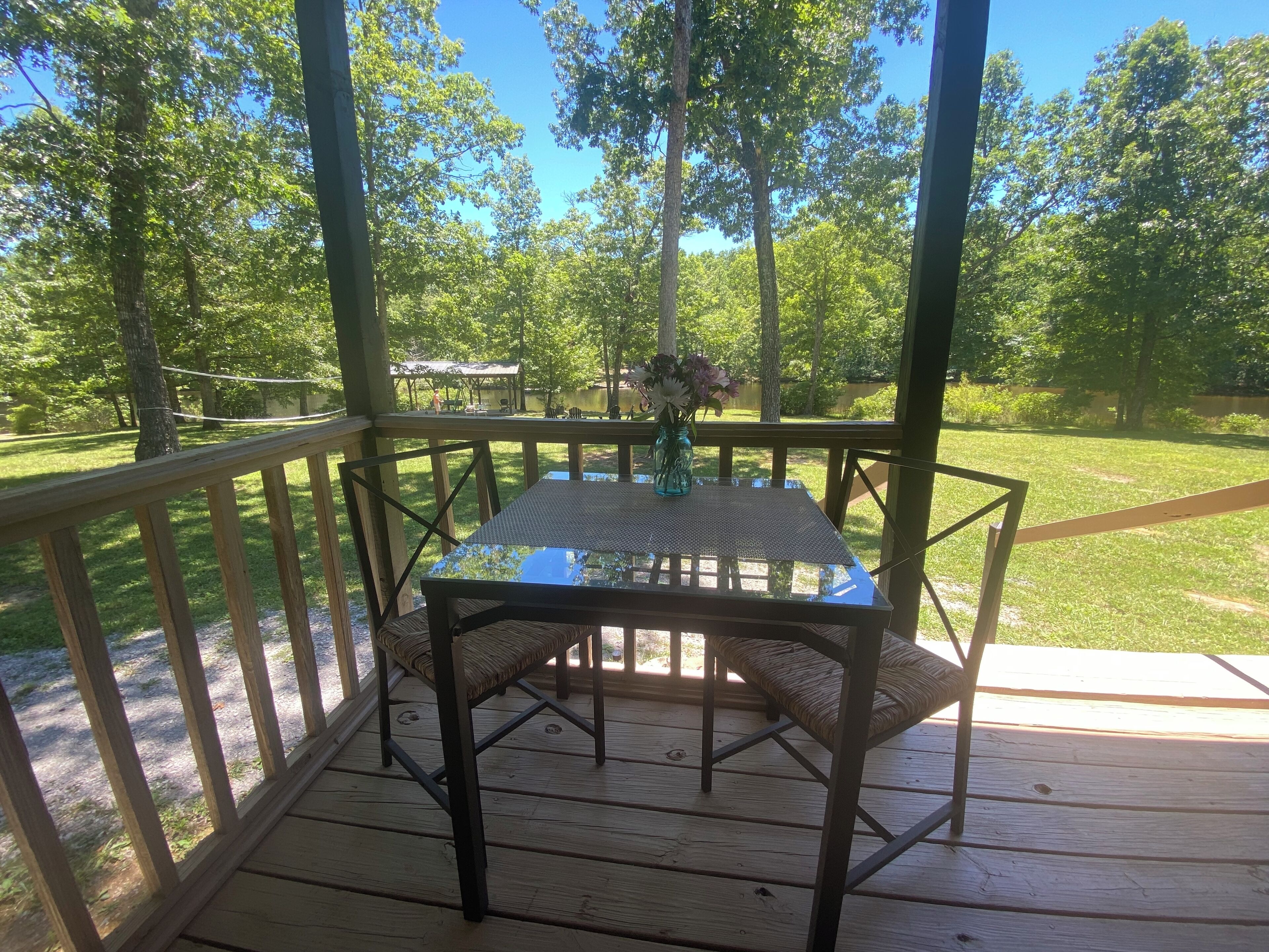 Un espacio al aire libre techado con una mesa y sillas, rodeado por una terraza de madera y una barandilla.