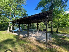A covered picnic area with tables and chairs, a barbecue grill, and a hammock.